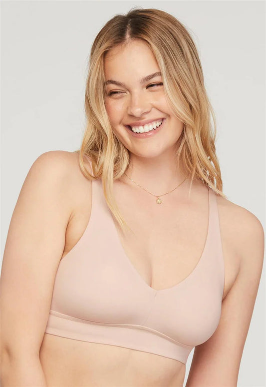 A woman wearing a light beige cup-sized bralette with a v-neckline and adjustable straps.