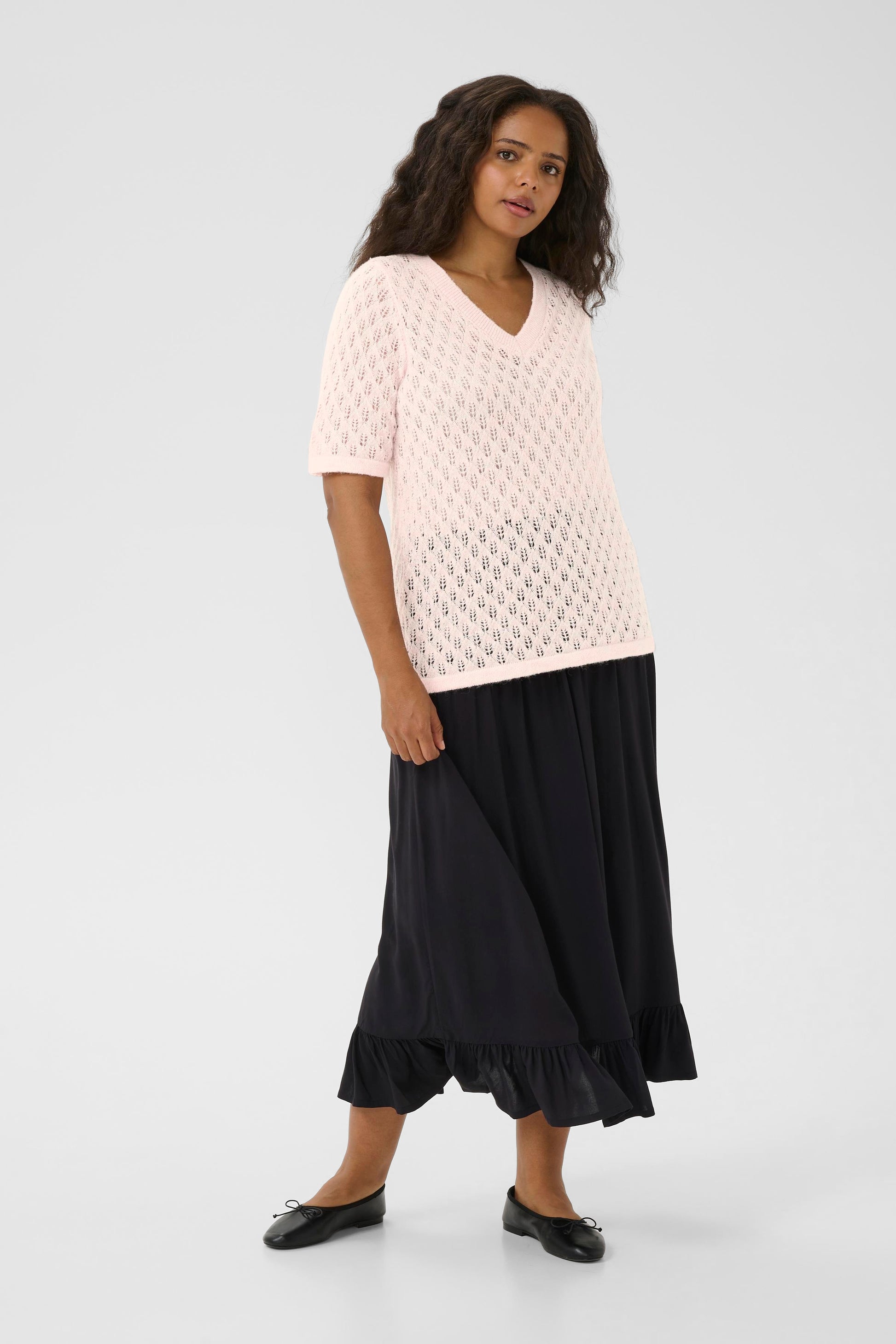 Woman wearing a light pink textured top and black skirt on a white background