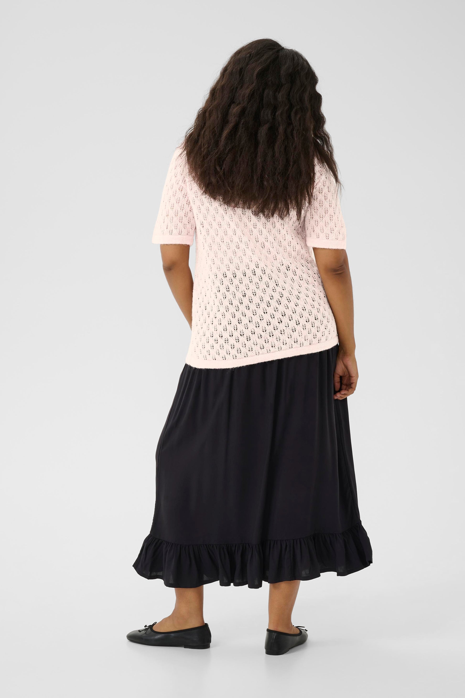 Person wearing a light pink top with a textured pattern and a black skirt on a white background