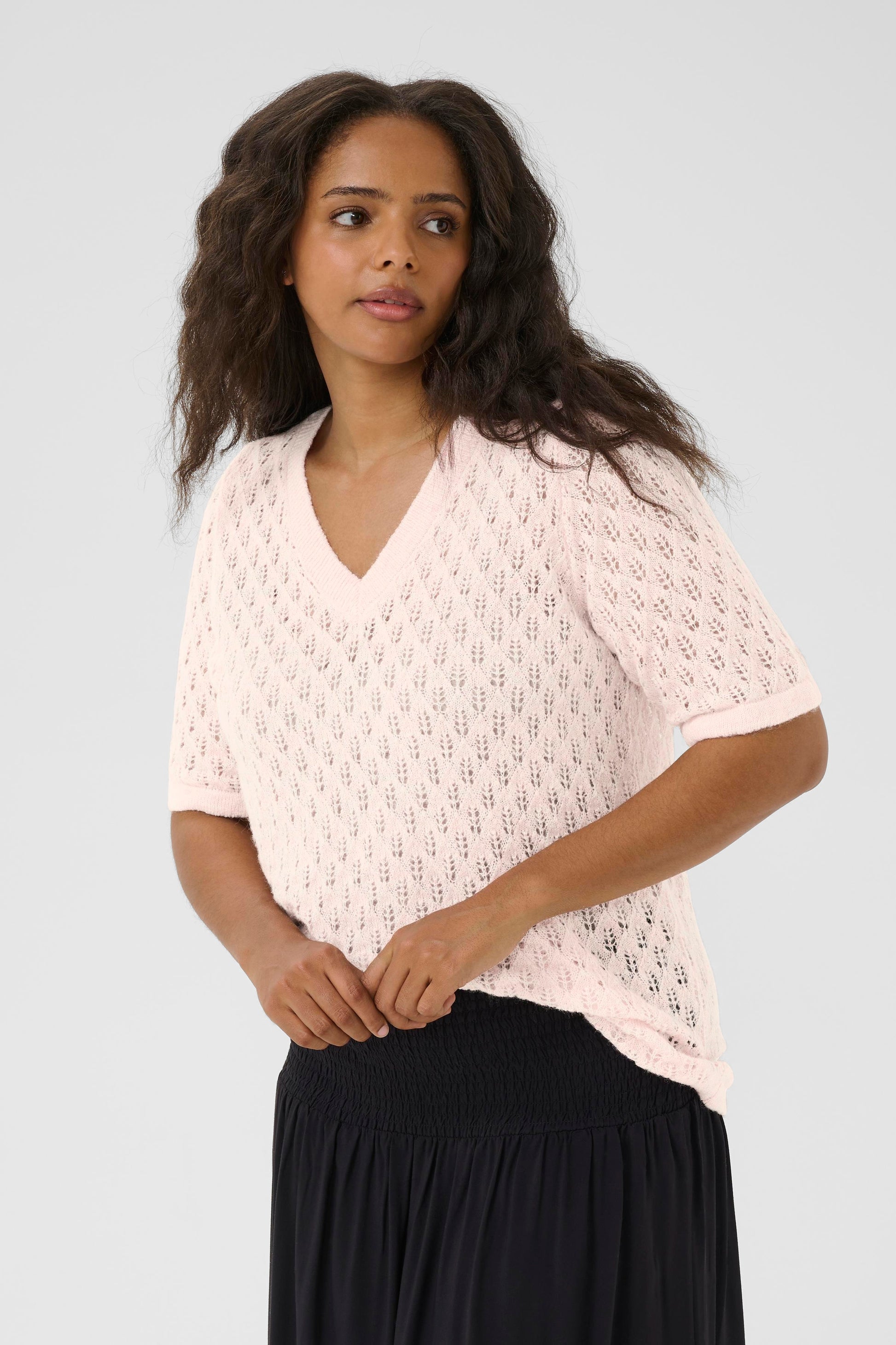 Woman wearing a light pink lace top and black pants on a white background