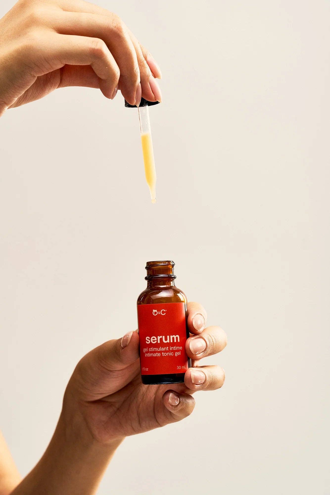 Hand holding a red serum bottle with dropper against a light background