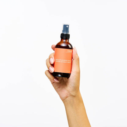 Plant-based intimate toy cleaner spray bottle labeled “Clean" held by a hand on a minimal background.
